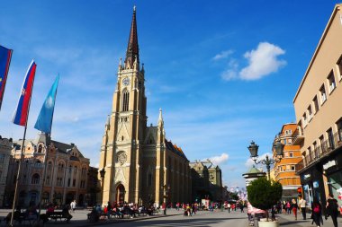 Freedom Square, Novi Sad, Sırbistan, 30 Nisan 2022. İnsanlar cadde boyunca yürür. Sırbistan ve Avrupa Birliği bayrakları dalgalanıyor. Adı Mary Church, Novi Sad 'daki Katolik kilisesi.