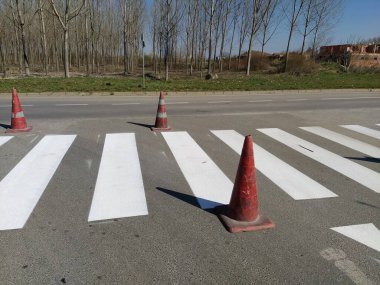 Painting pedestrian crossings with new paint. Road warning plastic orange cone. White stripes on the pavement. The pedestrian crossing is marked with special road signs or markings.