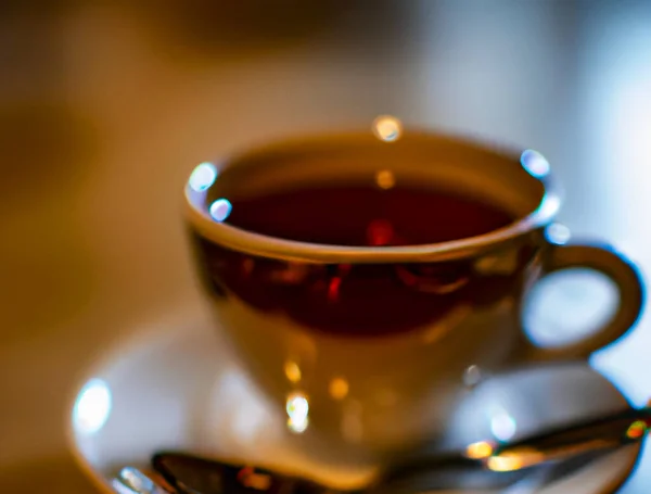 Cup of a hot tea in cafe. Anamorphic bokeh effect. Tilt-shift photo. Tasty aromatic tea in a lovely cup with a saucer. The tea is getting cold. Natural aroma. Label or advertisement. Evaporation