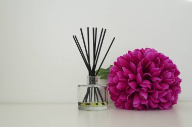 Tütsü çubukları, cam bir vazoda gerekli yağ ve beyaz bir odanın içinde parlak pembe leylak çiçekli suni bir çiçek. Beyaz arkaplan.