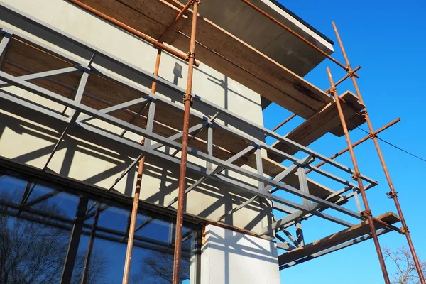 Scaffolding on a new one-story house. Facade works. Building bussiness. Low-rise private building. Plastering the wall of a building. Shop building. Metal production structures