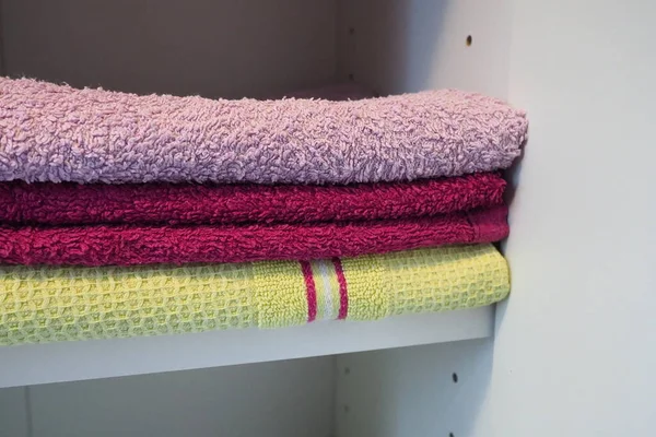 白色橱柜架子上的毛巾 干净的熨烫过的粉色和黄色毛巾叠成一堆 在浴室或壁橱中整理家用物品 家庭主妇的工作成果 — 图库照片