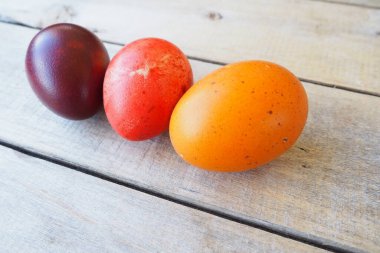 Paskalya renkli yumurtalar ahşap masaya yakın plan, paskal arka plan. Kırmızı, turuncu ve kahverengi kabuklu, soğan kabuğuyla boyanmış üç haşlanmış tavuk yumurtası.