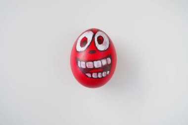 Paskalya yumurtası kırmızı, beyaz ve siyaha boyanmış neşeli dişli bir yüzle. Haşlanmış tavuk boyalı yumurta ve kırmızı kabuk. Beyaz arka plan. Büyük gözler, beyaz dişler ve eğlenceli bir yüz. Boşluğu kopyala.