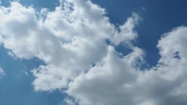 Zaman, bulutlu ve güneşli güzel mavi gökyüzünü hızlandırıyor. Bulutların hızlı hareketi. Açık beyaz bulutlar hızla akıyor. Ses ötesi ışık. Güneş ışınları