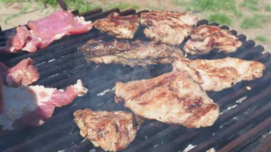 Izgarada ızgara ızgarada ızgara, alevler ve duman içinde ızgara etli domuz eti. Izgara sulu biftek hazır. Yeni et parçaları kızartma makinesine elle eklenir.