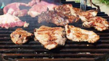 Izgarada ızgara ızgarada ızgara, alevler ve duman içinde ızgara etli domuz eti. Izgara sulu biftek piknik için hazır. Hazır mısın diye et parçalarını kontrol ediyorum. Taze et ekleniyor.