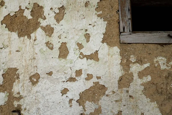The wall of a residential old house built with bricks made from mud, cow dung and straw. Peeling plaster. Serbia, ancient building technology. Texture of plaster and bricks. Window with wooden frame