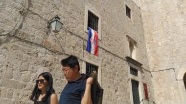 Dubrovnik, Hırvatistan, 08.14. 2022 gezi ve turizm. Hırvatistan 'ın ulusal bayrağı. Bayrak St. Dominic Caddesi 'ndeki bir pencereden asılmış. Antik taş manastır duvarları. İnsanlar ve turistler gider
