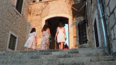 Herceg Novi, Karadağ, 08.10.2022 Sahat Kula bir saat kulesi, kareler arasında bir geçit. Bu popüler bir turistik ilgi odağı. Yazlık elbiseli üç kadın merdivenleri tırmanıyor. Turistler yürüyor