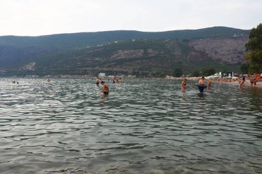 Herceg Novi Montenegro 08.09.2022 Deniz tatili Adriyatik gezisi Akdeniz seyahati. Rocky plage dağları. Sudaki dalgalar. İnsanlar yüzer, güneşlenir ve sahilde eğlenir. Sudaki kadın ve erkekler