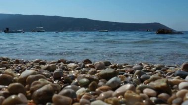 Deniz dalgaları kumsalda çakıl taşları. Çakıl taşlarını yıkayan bir deniz dalgasının güzel yakın plan görüntüleri. Karadağ 'daki Rocky Plage, Herceg Novi. Temiz suyun hareketi. Yaz okyanus tatili. Yuvarlak çakıl.