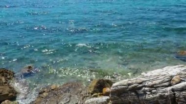 Şeffaf deniz tuzlu su dokusu. Su yüzeyinin üst görüntüsü ve dalgalanmalar. Su dalgaları arka planda. Alglerle kayalık taban. Su sıçratan dalgalar kayalara çarpıyor. Karadağ, Herceg Novi.