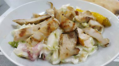 Sezar sebze salatası. Popüler bir Amerikan yemeği. Restoranda beyaz bir tabakta sebze salatası ve ızgara tavuk. Dilimlenmiş salatalık, domates, marul, mayonez ile karıştırılmış tavuk parçaları..