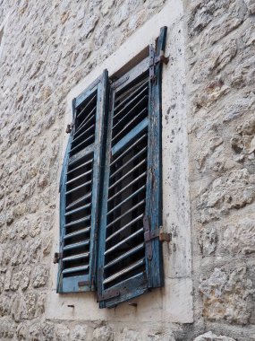 Eski bir evin üzerinde yeşil kepenkleri olan eski pencere. Eskimiş doku. Herceg Novi, Karadağ, eski taş ev. Adriyatik bölgesinin mimarisi. Pencereler ve panjurlar tamir ediliyor.