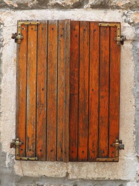 Eski bir evin üzerinde kırmızı kahverengi kepenkleri olan eski pencere. Eskimiş doku. Herceg Novi Montenegro, eski taş ev. Adriyatik bölgesinin mimarisi. Pencereler ve panjurlar tamir ediliyor.