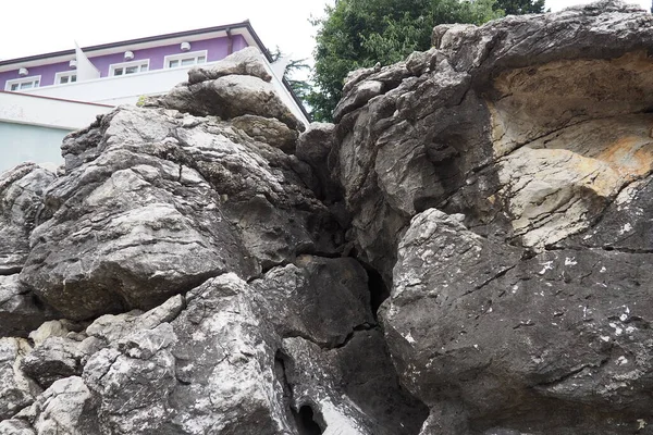 House hotel on the edge of a rock, hardened volcanic lava. Herceg Novi, Montenegro. A large crevice in the rock, a cave. Layers in a rock. Geology and seismology in the Adriatic Mediterranean region.