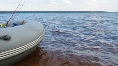 Lososinnoye Gölü kıyısındaki dalgalarda şişme bir tekne sallanıyor, Karelia. Balık oltaları olta takımı. Mavi saat akşamı. Su hareketi ağır çekim. Dalgalar ve dalgalar. Bulutlu hava.