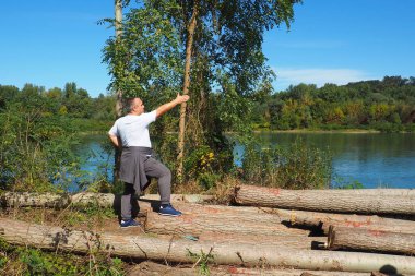 Drina Reka Sırbistan Banja Koviljaca 30 Eylül 2022 'de nehir kıyısında kereste işi yaptı. Adam yalan kayıtlarını eliyle işaret ediyor. Orman mühendisliği endüstrisi. Tarıma elverişli topraklar için ağaçları kesiyorlar..