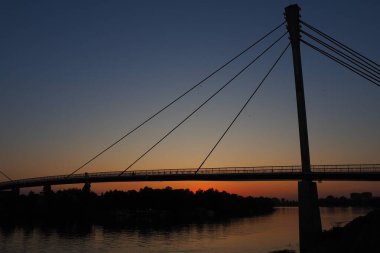Sava nehri üzerindeki Saint Irinej Köprüsü. Avrupa 'nın en uzun yaya-bisiklet köprüsü Sremska Mitrovica ile Macvanska Mitrovica arasında yer almaktadır. Karşıt kıyılardaki ikiz kasabalar. Gün batımı