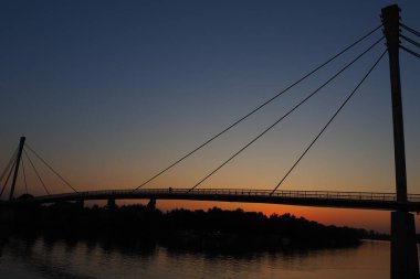 Sava nehri üzerindeki Saint Irinej Köprüsü. Avrupa 'nın en uzun yaya-bisiklet köprüsü Sremska Mitrovica ile Macvanska Mitrovica arasında yer almaktadır. Karşıt kıyılardaki ikiz kasabalar. Gün batımı
