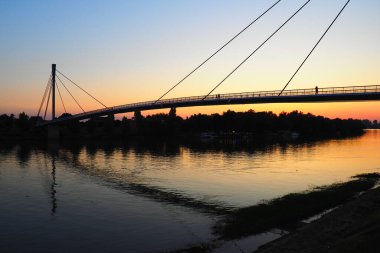 Sava nehri üzerindeki Saint Irinej Köprüsü. Avrupa 'nın en uzun yaya-bisiklet köprüsü Sremska Mitrovica ile Macvanska Mitrovica arasında yer almaktadır. Karşıt kıyılardaki ikiz kasabalar. Gün batımı