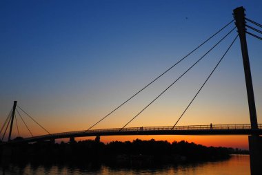 Sava nehri üzerindeki Saint Irinej Köprüsü. Avrupa 'nın en uzun yaya-bisiklet köprüsü Sremska Mitrovica ile Macvanska Mitrovica arasında yer almaktadır. Karşıt kıyılardaki ikiz kasabalar. Gün batımı