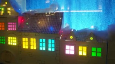 Theatrical showcase with a cute childrens winter New Years town. Houses with colored windows. Flashing holiday garlands. The glare of car headlights is reflected in the glass. Christmas decorations.