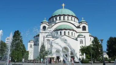Belgrad, Sırbistan, 9 Eylül 2023 St. Sava Kilisesi, bir Sırp Ortodoks Tapınağı. Muhteşem çan kuleleri. Çeşmeye su sıçrıyor. Turistler ve inançlı insanlar tapınağın önünde yürürler..