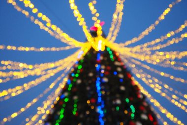 Multi-colored glass shiny balls on the New Years city tree. Glowing garlands hang over the Christmas tree. Outdoor winter decoration. Festive design of the city square. Red, blue and yellow ball.