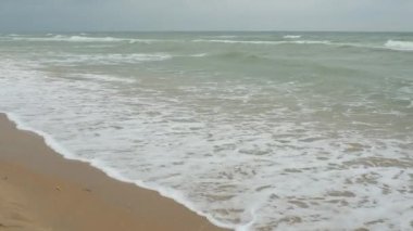 8 yaşında bir kız çocuğu kumsalda suya doğru yürüyor, soğuktan titriyor ve dalgalara bakıyor. Sakin dalgalar kumlu sahilde yuvarlanıyor. Dalgalar köpükten köpürüyor. Turizm ve rahatlama.