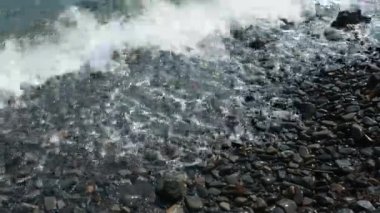 Okyanus dalgaları kumsaldaki çakıl taşlarını ezer. 4K deniz dalgaları kıyıya çarpıyor. Bir tutam deniz fırtınası köpüğü. Dev dalgalar kıyı kayalarına çarpıyor. Kafkas Dağları Sukko Karadeniz