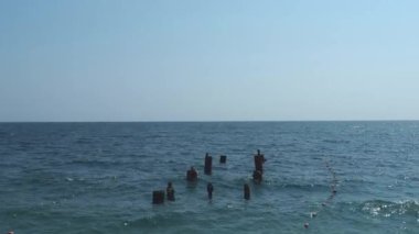 Derin denizin arka planına karşı iskele mahvoldu. Ahşap direkler mavi sulardan sarkıyor. Güneşli havada Karadeniz. Yazın bulutsuz gökyüzü. Tuzlu deniz suyunda küçük dalgalar. Navigasyon, turizm