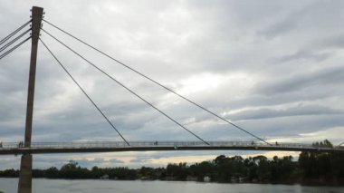 Sremska Mitrovica Sırbistan 10.28.2023 Sremska Mitrovica ve Sava Nehri. St. Irineja 'dan Macvanska Mitrovica' ya yaya köprüsü. İnsanlar nehrin üzerindeki asma köprü boyunca yürüyüp bisiklete biniyorlar..