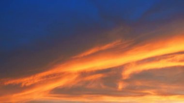 Sarı turuncu mavi günbatımı gökyüzü bulutları. Sarının yumuşak, ılık tonu huzurlu bir atmosfer yaratıyor. Batan güneşin yumuşak ışınları ufku boyar. Güzel bir zaman atlaması. Hava tahminleri