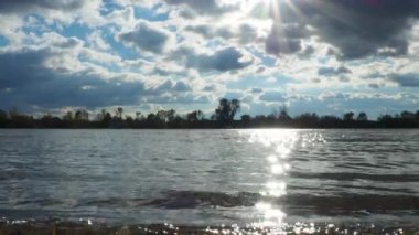 Nehir akış rotası. Kaynağından ağzına kadar doğal akış. Sakin su, dalgalar yüzey dokusunu dalgalandırır. Sava Nehri Sırbistan. Bulutlar ve güneş. Güneş ışınlarının suya yansıması. Sonbahar havası