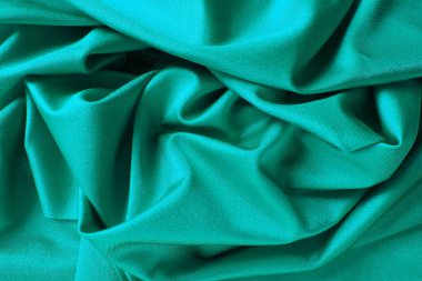 Yeşil ipek kumaş dokusu arka planı. Merkeze doğru bükülmüş materyalin güzel kıvrımları. Kumaşta yumuşak bir parıltı.