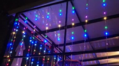 Yanan çelenk. Terasta ya da verandada çok renkli ampuller yanıyor. Yılbaşı gecesi. Sokak lambası. Bina dekorasyonu. Güzel kırmızı, mavi, yeşil çelenkler gece kafede