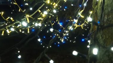 Noel ağacının üzerinde parıldayan altın çelenkler asılı. Açık hava kış dekorasyonu. Şehir meydanının şenlikli tasarımı. Çelenkler yanıp sönüyor. Bokeh yanıp sönen ampuller. Noel Xmas Festivali.