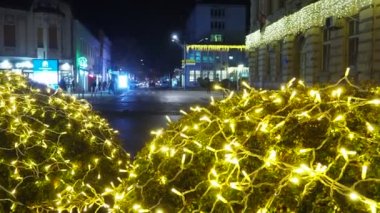 Sırbistan 'ın Sremska Mitrovica kenti, 12,12,23: Altın çelenk parıldayan Noel Yeni Yılı. Kış dekorasyonu. Şenlikli tasarım şehir meydanı. Noel Xmas Festivali. Arabalar sürüyor, insanlar sokakta yürüyor.