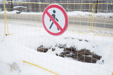 Geçiş işareti yok, geçmeyin. Kırmızı çizgili bir adam. Yuvarlak yasaklı yol tabelası. Yasak. Metal bir çitle çevrili bir çukur. Kış, kar ve yol kenarında kar yağışı.