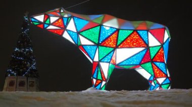 Ayı çelengi. Çok renkli, ışıl ışıl parlayan yeni yıl ayısı geceleri kar üzerinde. Kurulum figürü, tatilde sokakları dekore etmek için mimari form. Kırmızı, mavi, yeşil, beyaz üçgen..