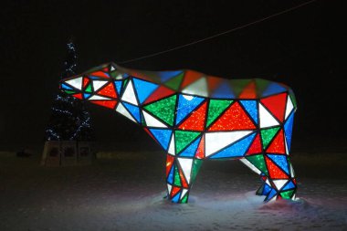 Ayı çelengi. Çok renkli, ışıl ışıl parlayan yeni yıl ayısı geceleri kar üzerinde. Kurulum figürü, tatilde sokakları dekore etmek için mimari form. Kırmızı, mavi, yeşil, beyaz üçgen..