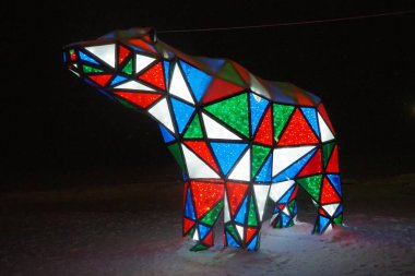 Ayı çelengi. Çok renkli, ışıl ışıl parlayan yeni yıl ayısı geceleri kar üzerinde. Kurulum figürü, tatilde sokakları dekore etmek için mimari form. Kırmızı, mavi, yeşil, beyaz üçgen..