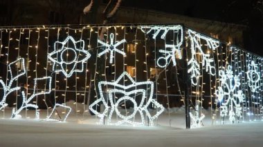 Parlayan kar taneleri. Yeni yıl şenlikli Noel elektrik sanatı tesisatı kar yığınındaki mimari yapılar. Şehir sokağının hafif dekorasyonu. Kış gecesi. Çelenk ampulleri gümüş renginde parlıyor. Xmas.