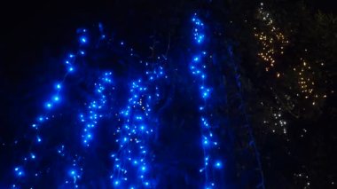 Noel ağacının üzerinde parlayan mavi çelenkler asılı. Açık hava kış dekorasyonu. Şenlikli şehir tasarımı. Çelenkler yanıp sönüyor. Çözülmüş bokeh titreyen ampuller. Noel Xmas Festivali Keyfi yerinde.