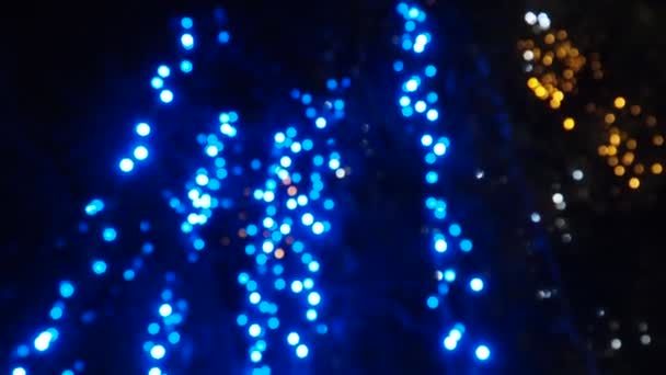 新しい輝く青いガーランドはクリスマスツリーの上にぶら下がります 屋外の冬の装飾 お祝いの都市デザイン ガーランドが点滅し 揺れる 電球を点滅させるボケを分割しました フェスティバルノエルXmas良い気分 — ストック動画