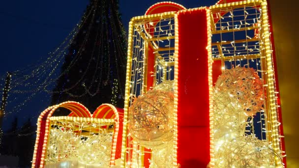 金色の赤いガーランドの電球から成っている大きい弓が付いている明るいギフト用の箱の形の建築様式 都市の通りや広場の装飾を祝う クリスマスと新年 クリスマスナイト — ストック動画