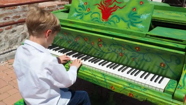 一个穿着白衬衫的金发男孩在街上弹钢琴 那个9岁的白人小孩钢琴漆成绿色 音乐表演 街头音乐会 广场上的暴民音乐精湛 — 图库视频影像