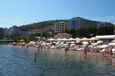 Budva, Karadağ 08.15.22 Pebble plajı. Plaj şemsiyeleri, kafeler, şezlonglar. İnsanlar rahatlar, yüzer, güneşlenir. Turizm sektörü Balkanlar. Halk plajı. Otel ve apartmanlar